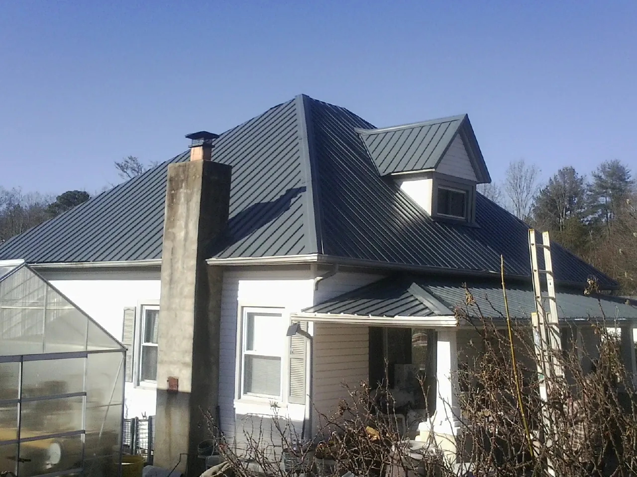 Dark blue standing seam metal roof on a white farmhouse with dormer — Slate & Tile Roof Repair by Roofing Brothers in Malibu