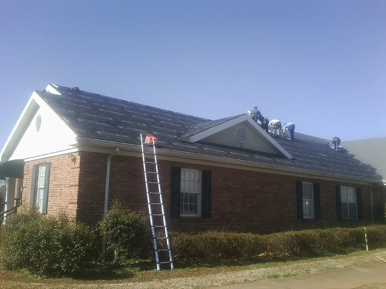 Crew tearing shingles off a brick ranch roof with a ladder set — Emergency Roof Repair work by our crew in Malibu